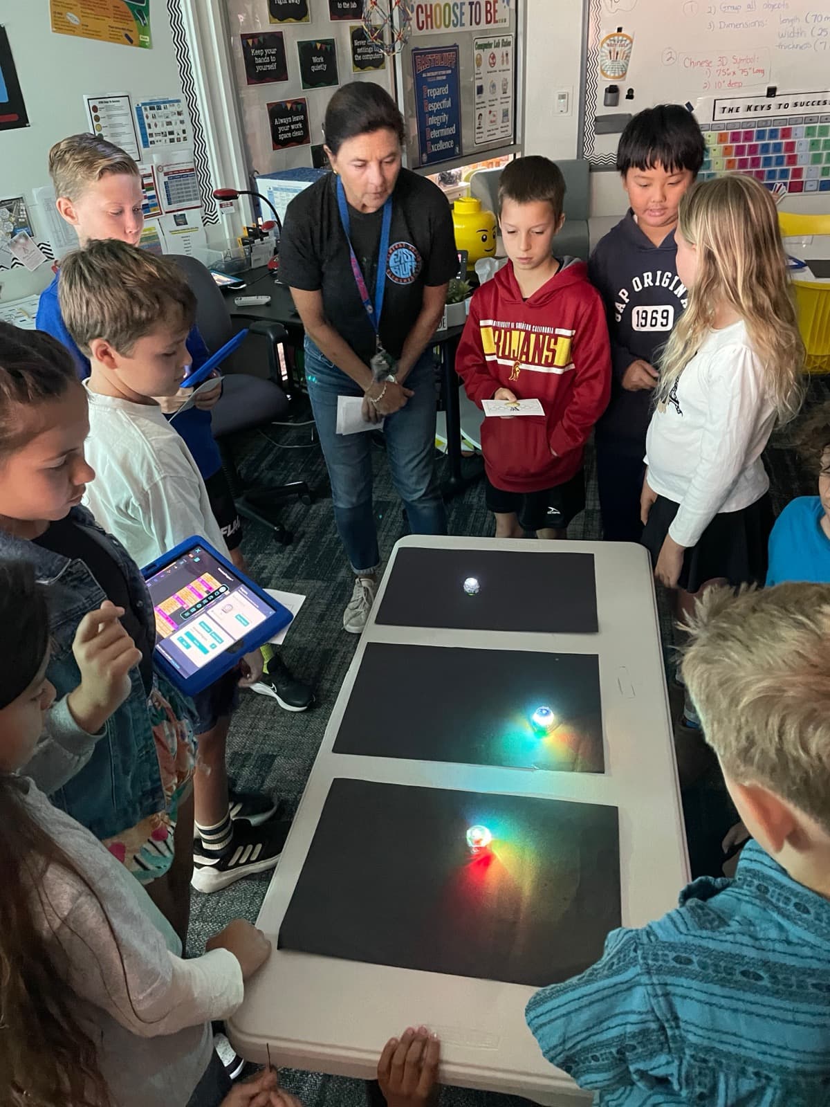 Eastbluff students and Mrs. Mannon watching programmable robots light up on a table